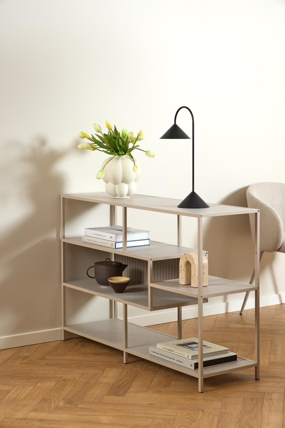 Light wooden shelf with books, a vase of flowers, and a lamp against a white wall.