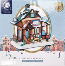 Load image into Gallery viewer, Mini World Collectibles light-up ski school resin collectible in its original packaging, featuring a detailed wooden house with a snowy roof, miniature characters, and a winter town illustration.
