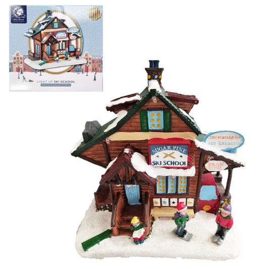 A decorative miniature village building labeled 'Sugar Pine Ski School' on a snowy base, shown with its retail box inset in the upper left. The scene includes small figurines, a red car, and winter-themed signage on a plain white background.