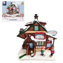 Load image into Gallery viewer, A decorative miniature village building labeled 'Sugar Pine Ski School' on a snowy base, shown with its retail box inset in the upper left. The scene includes small figurines, a red car, and winter-themed signage on a plain white background.
