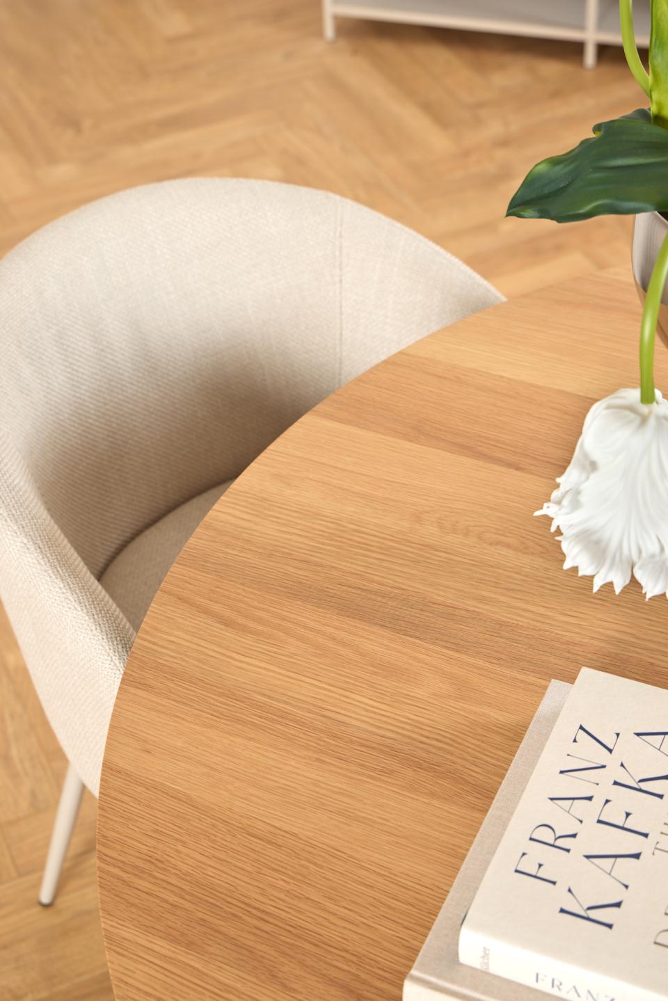 Round wooden Soli table with a book and a white flower on a wooden floor.
