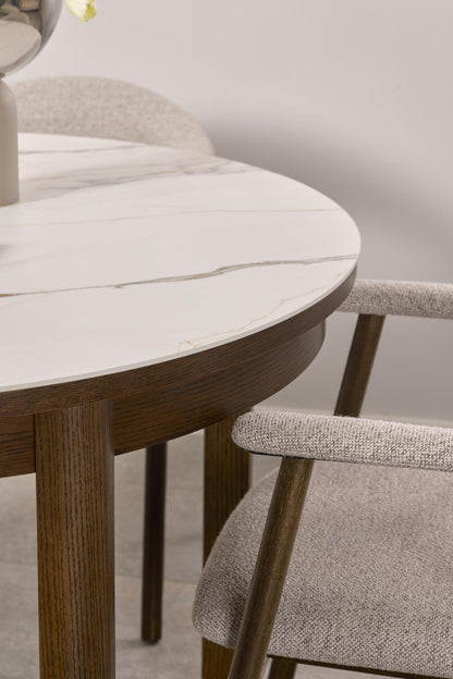 Round wooden dining table with marble top and matching chairs in a neutral setting