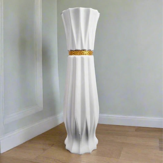 A white ceramic floor-standing vase with a gold stripe detail, displayed against a soft-focus background.