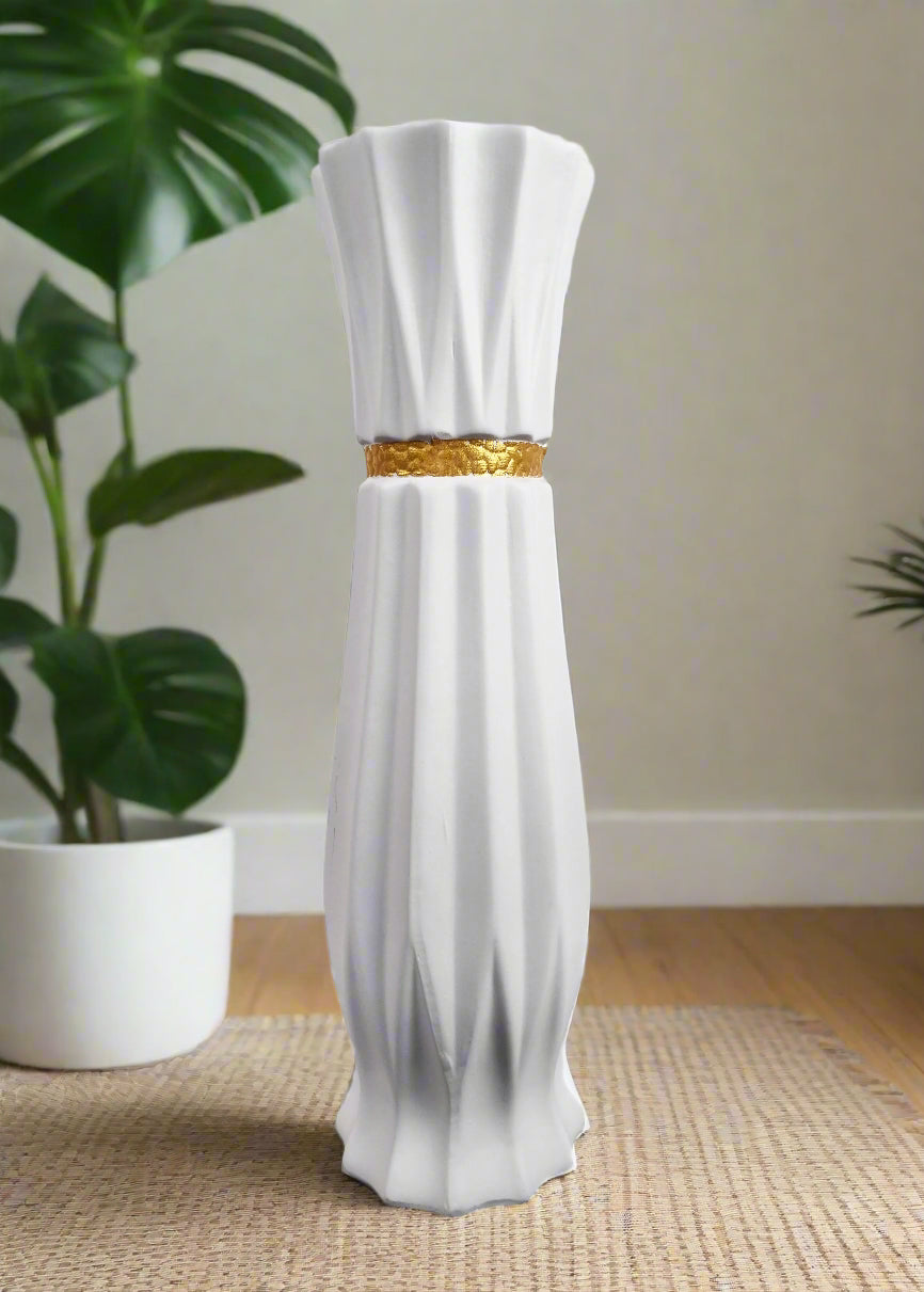 a white ceramic vase with gold stripe in a home with a plant in the background