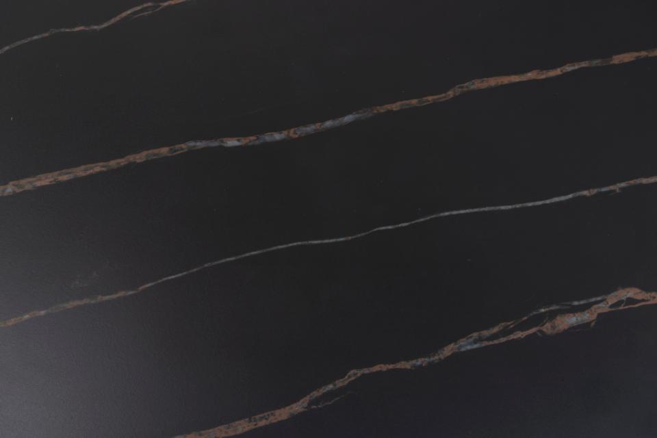 A close-up of a dark polished stone surface, likely black marble or similar, with thin warm metallic veining running diagonally across the frame.