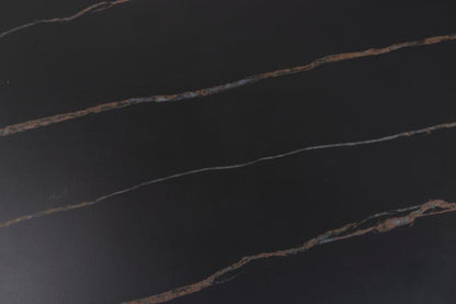 A close-up of a dark polished stone surface, likely black marble or similar, with thin warm metallic veining running diagonally across the frame.
