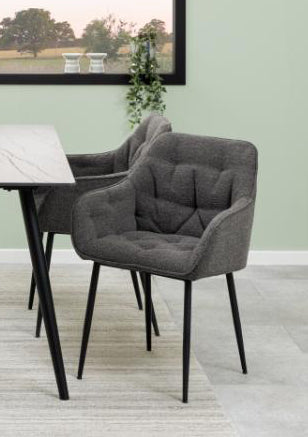 Two upholstered dining chairs in dark gray fabric with black metal legs, shown beside a white marble-top table in a styled interior setting.