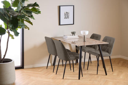 A modern dining set featuring a rectangular table with a light marble-patterned top and black metal legs, surrounded by four gray upholstered chairs with black legs. The set is styled in a bright room with beige walls, a herringbone wood floor, a large potted plant, and a framed print on the wall.