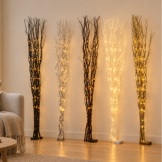 Five illuminated willow twig branches with tall clusters of thin branches and warm white string lights, styled in a modern living room next to a beige sofa and wooden cabinet.