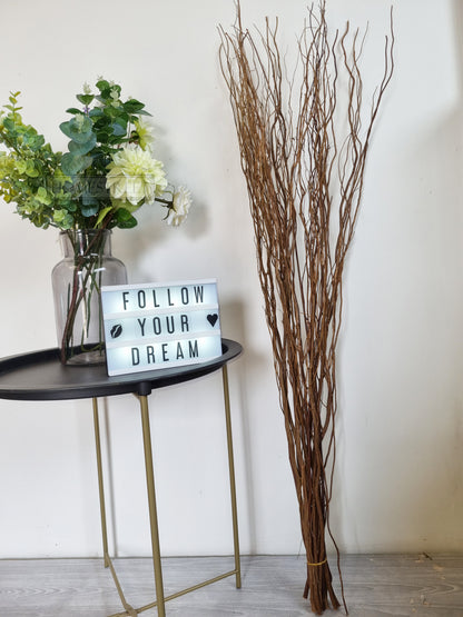 brown willow twig bunch next to artificial flowers in a home with a home decor sign