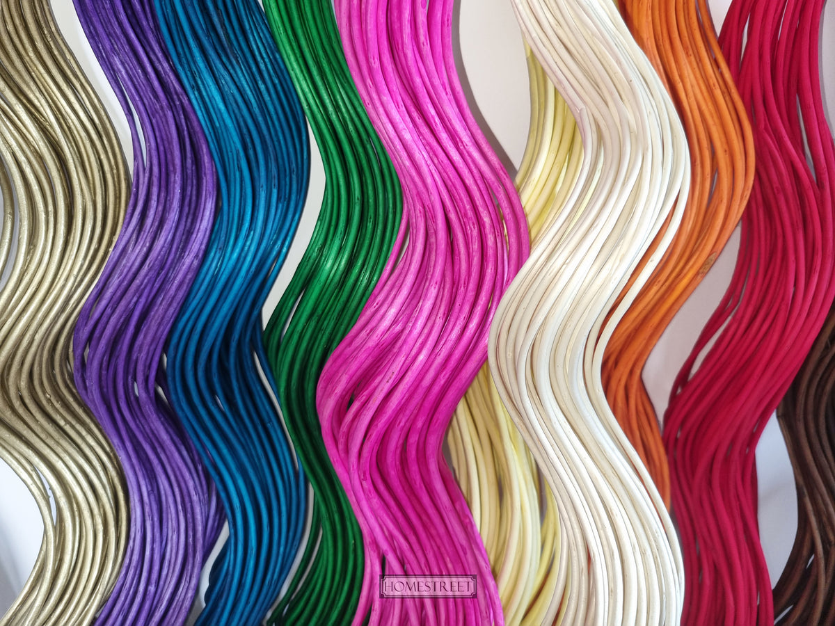 A close-up of multiple wavy strands of willow twig spiral shapes shown in different colors, including beige, purple, teal, green, hot pink, cream, pale yellow, orange, red, and brown, arranged vertically side by side.