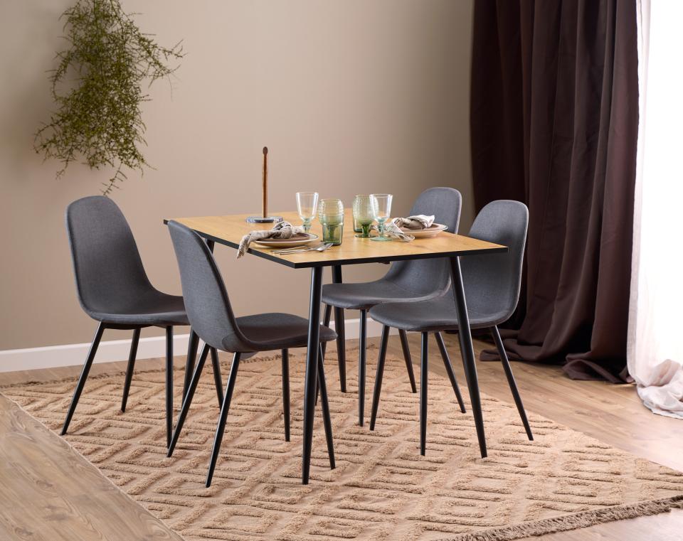 A modern 4-piece dining set featuring a rectangular light wood table with black metal legs and four gray upholstered chairs, styled on a textured beige rug in a dining room setting.
