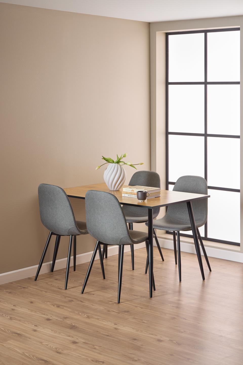 A modern dining set featuring a rectangular light wood table and four gray upholstered chairs with black metal legs, styled in a minimalist room with beige walls and light wood flooring.