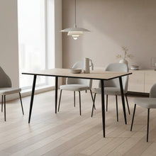 Load image into Gallery viewer, A rectangular dining table with a light beige wood-grain tabletop and four tapered black metal legs, shown against a plain white background.
