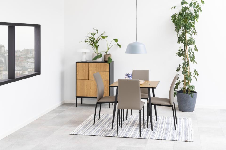 A modern dining set featuring a rectangular light wood table and four beige upholstered chairs with black metal legs, arranged on a striped gray and white rug in a bright, minimalist dining room.