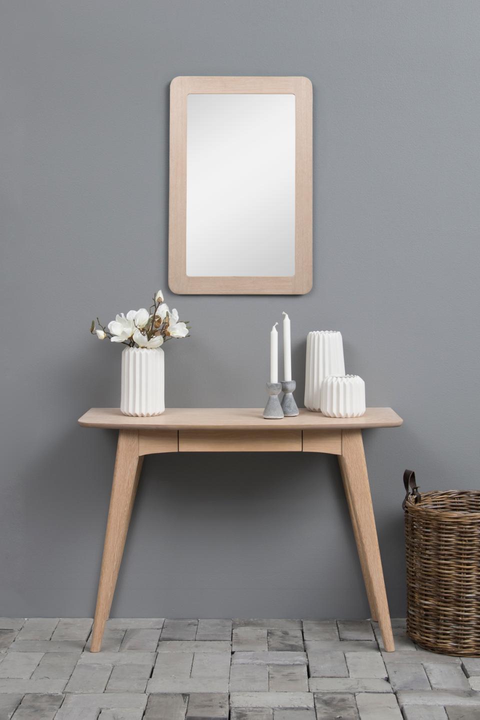 Wooden console table with mirror, candles, and decorative items against a gray wall.