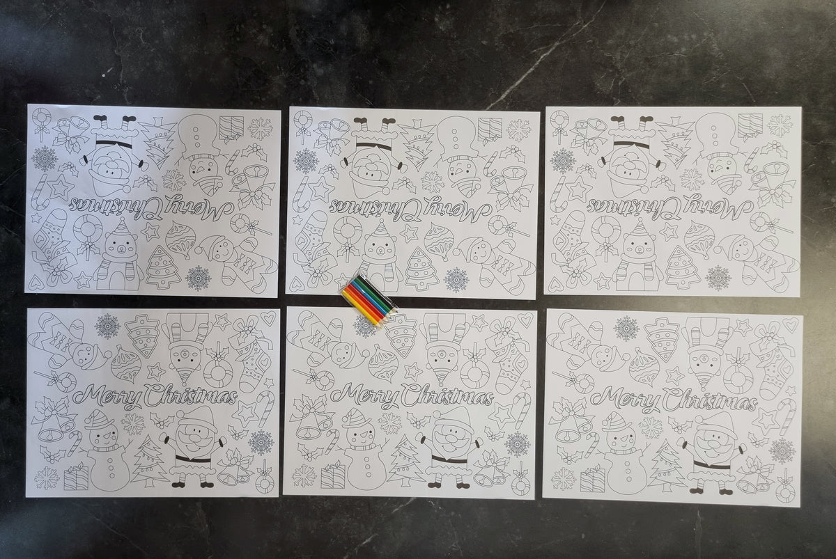 Six white Christmas-themed coloring pages arranged in a 2x3 grid on a dark gray marble surface. Each page features black line art of festive characters, snowflakes, ornaments, and the words 'Merry Christmas' in cursive.