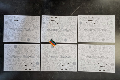 Six white Christmas-themed coloring pages arranged in a 2x3 grid on a dark gray marble surface. Each page features black line art of festive characters, snowflakes, ornaments, and the words 'Merry Christmas' in cursive.
