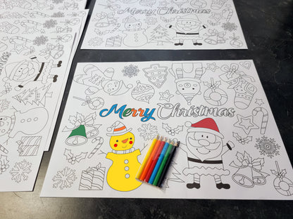 Three Christmas-themed coloring pages laid out on a dark countertop, with a set of colored pencils placed on the front page. The pages feature black-and-white outlines of Santa Claus, snowmen, ornaments, candy canes, and the text 'Merry Christmas.