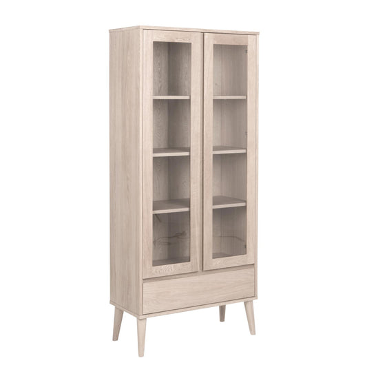 A tall, narrow light oak wood display cabinet with two glass doors, four interior shelves, and tapered legs, shown against a plain white background.