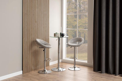 A pair of Plump taupe grey leather bar stools in a modern room by a window with a tall curtain